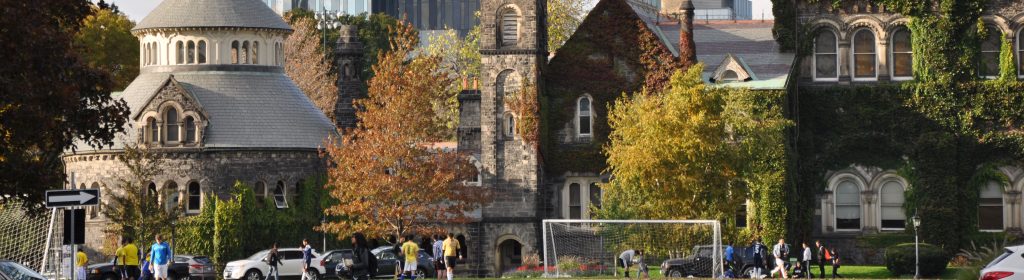Exterior of University college in fall season, with students playing soccer in front